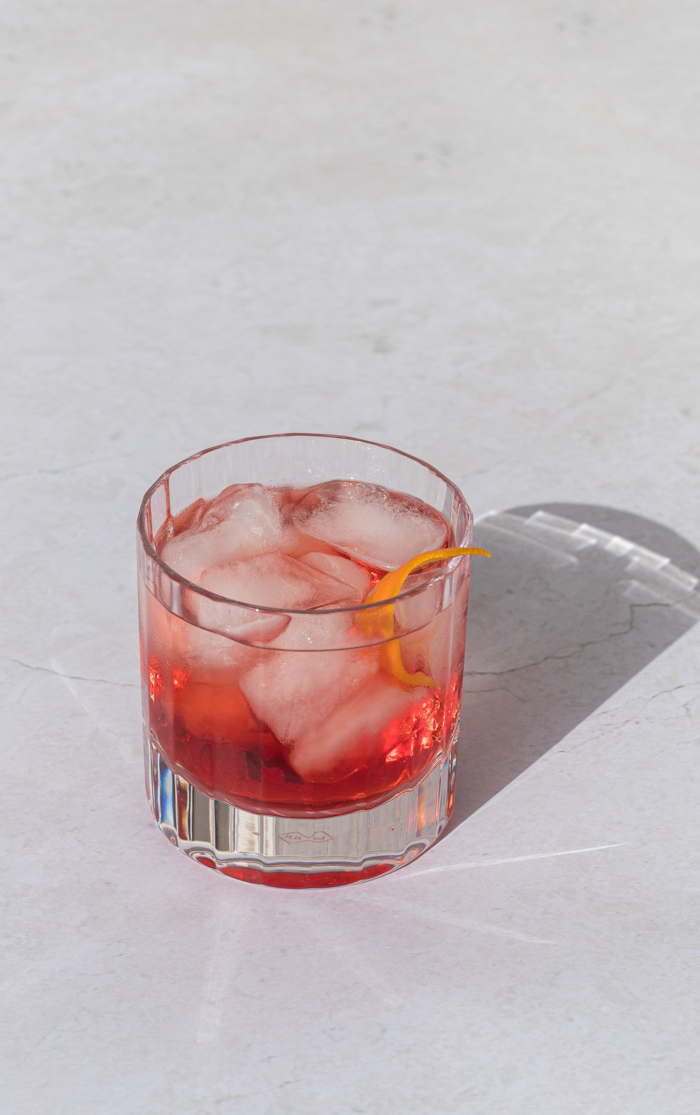 Clear fluted double old fashioned glass with red drink and ice on white background.