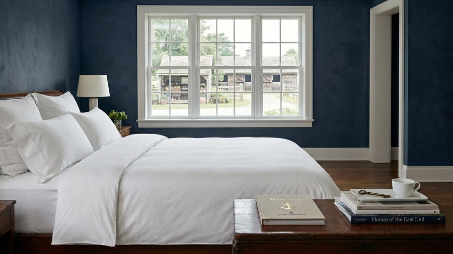 Bedroom with white bedding and a window showing a view of houses outside.