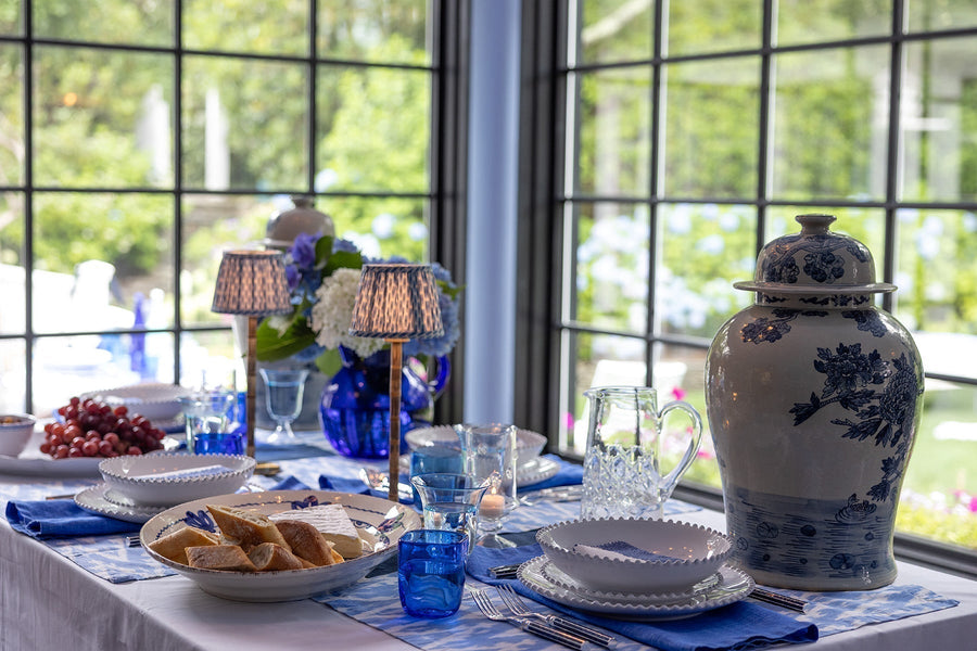 Elegant table setting with blue and white decor, including a vase and glasses, in a bright room.