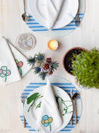 Table setting of two white plates and circular blue stripe placemats with green plant