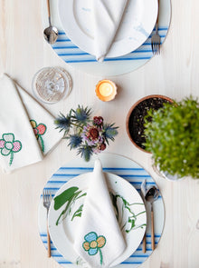 Table setting of two white plates and circular blue stripe placemats with green plant
