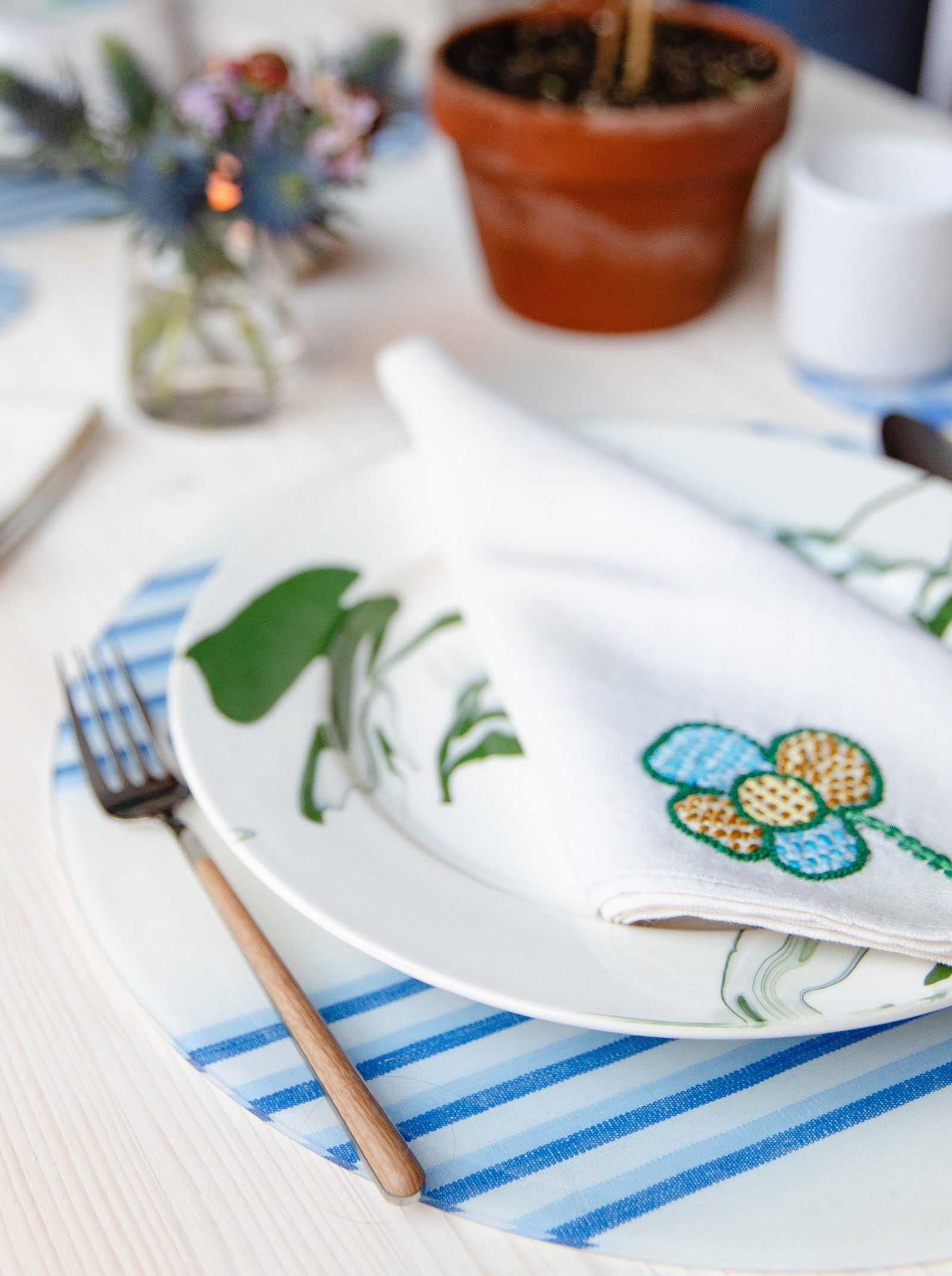 Dining table setting with a plate, fork, and embroidered napkin on a striped placemat.