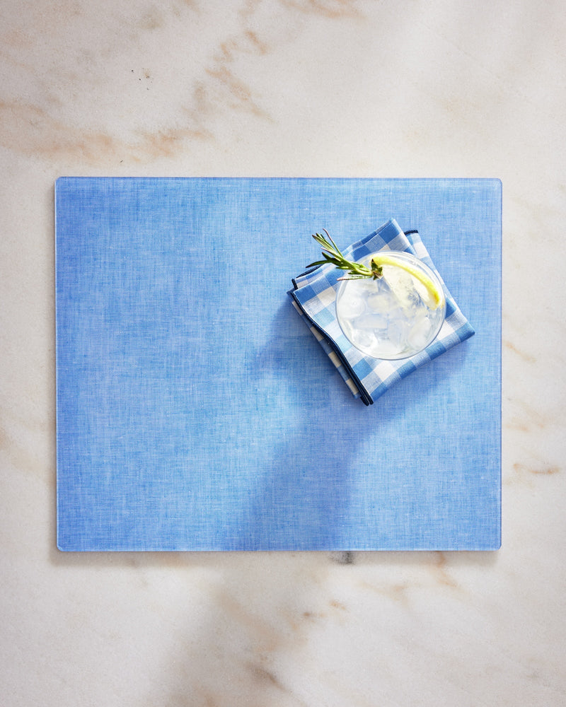 Blue placemat with a glass of water and folded napkin on a marble surface