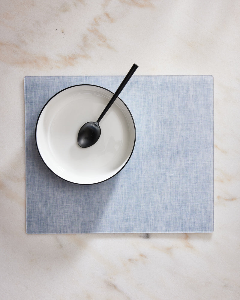 White plate with a black spoon on a blue placemat over a marble surface