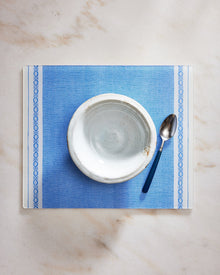 Blue placemat with a white bowl and spoon on a marble surface