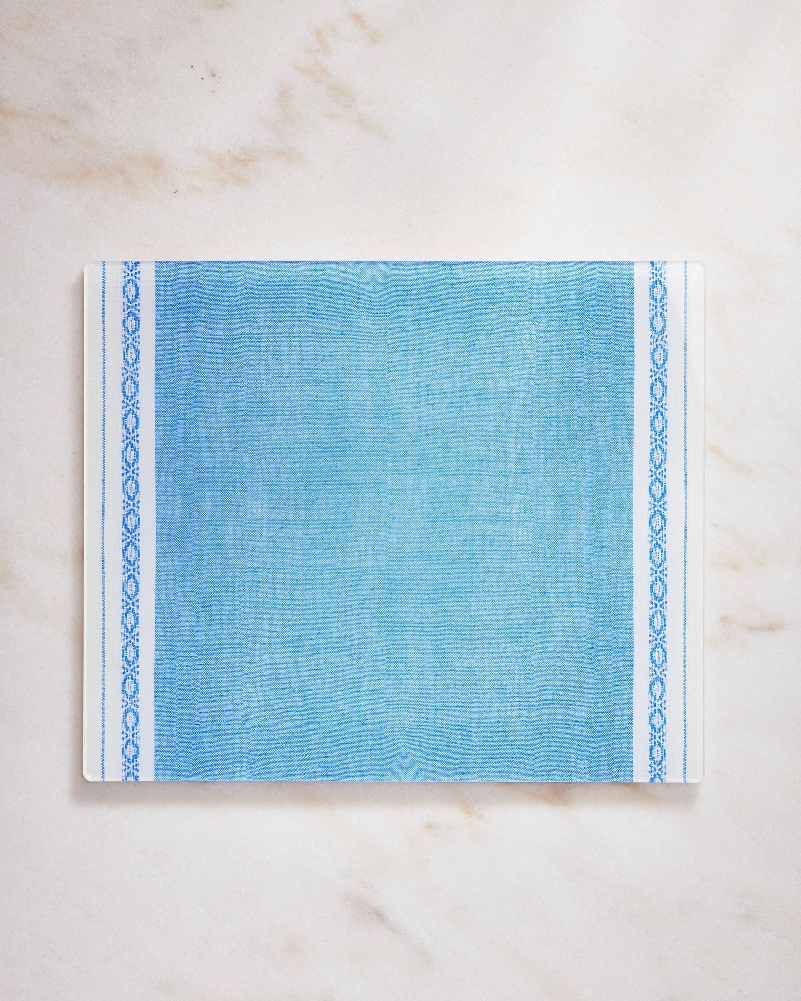 Blue fabric placemat with decorative border on a marble background