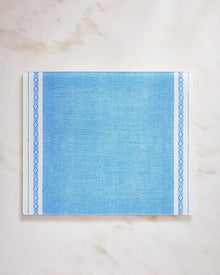 Blue fabric placemat with decorative border on a marble background