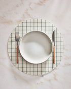 CIrcular placemat with green grid pattern on a marble surface