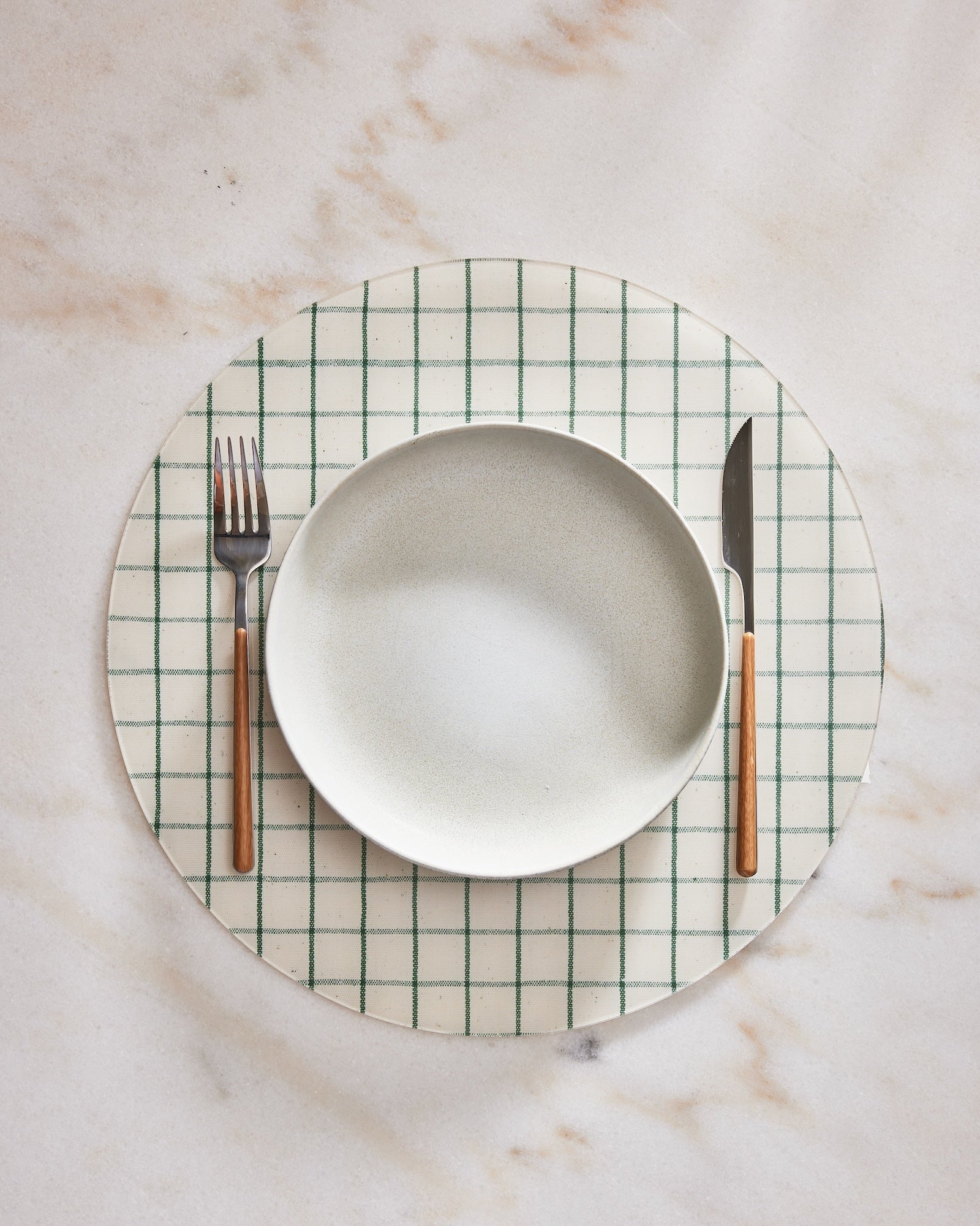 CIrcular placemat with green grid pattern on a marble surface