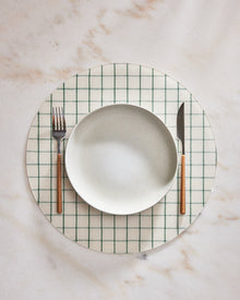 CIrcular placemat with green grid pattern on a marble surface