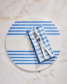 Round plate with blue stripes, checkered napkin, and cutlery on a marble surface