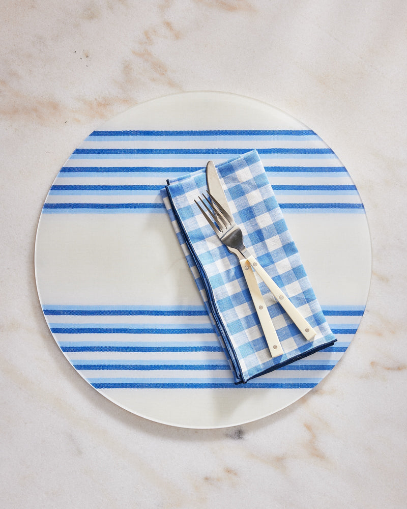 Round plate with blue stripes, checkered napkin, and cutlery on a marble surface