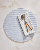 Round striped placemat with a folded napkin and cutlery on a marble surface