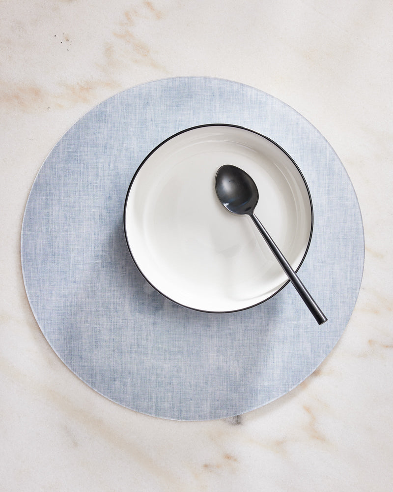 White bowl with black spoon on a gray placemat on a marble surface
