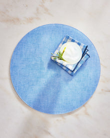 Round blue placemat with a small dish and napkin on a marble surface