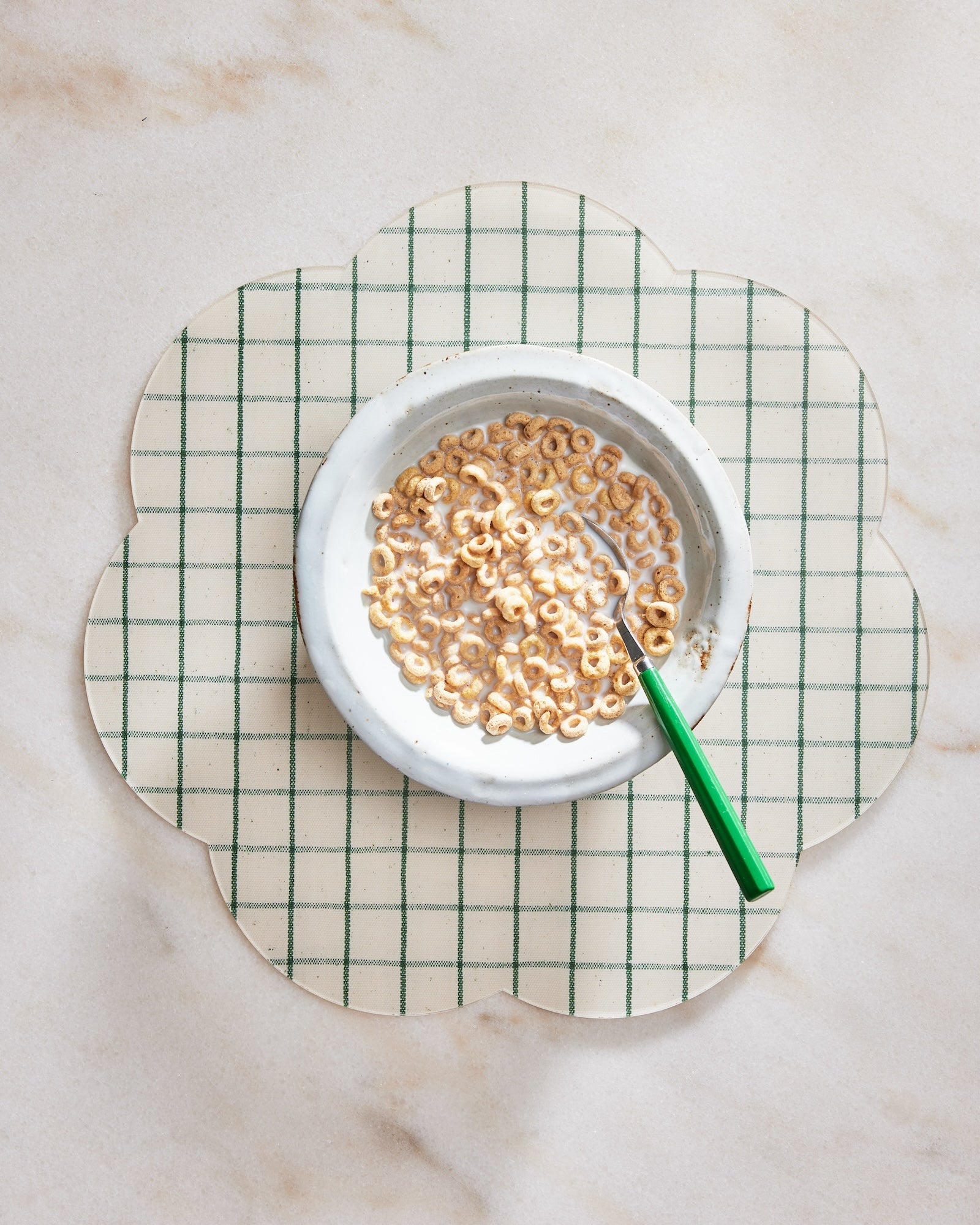 White bowl with cereal on a green and white checkered placemat on a marble surface