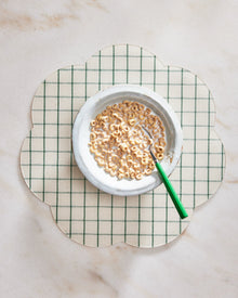 White bowl with cereal on a green and white checkered placemat on a marble surface