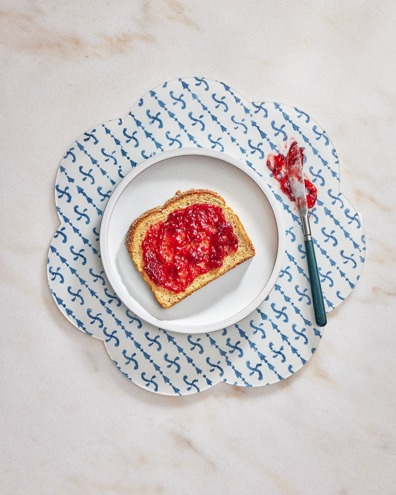 Toast with jelly on a white plate with a blue anchor patterned placemat on a marble surface.