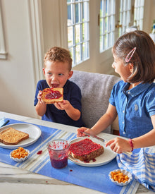 Two children at a table with toast and jelly, one child is eating toast with jelly.