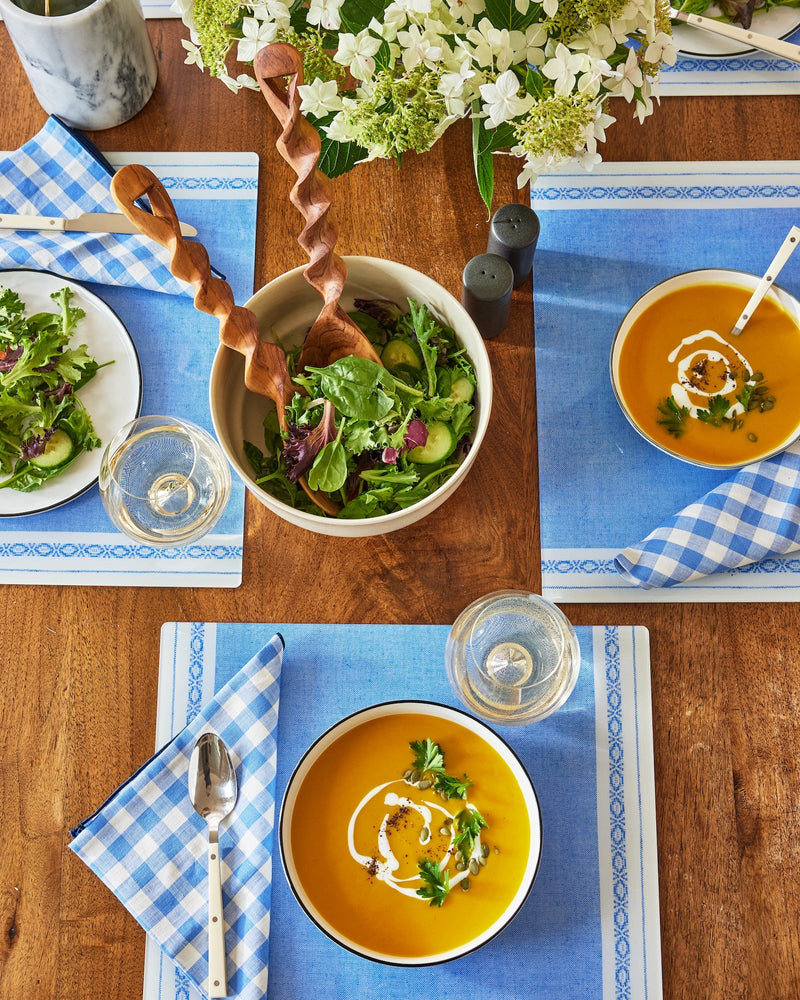 Two bowls of soup and a salad on a wooden table with blue checkered placemats.
