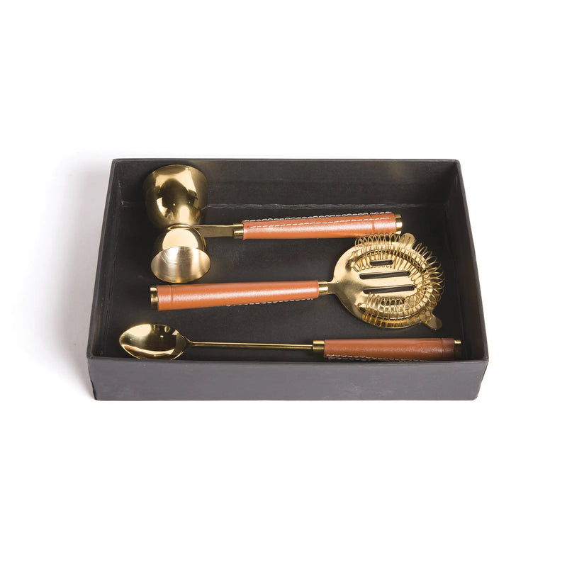 A set of gold-colored brass bar tools with leather handles, including a jigger, strainer, and spoon.
