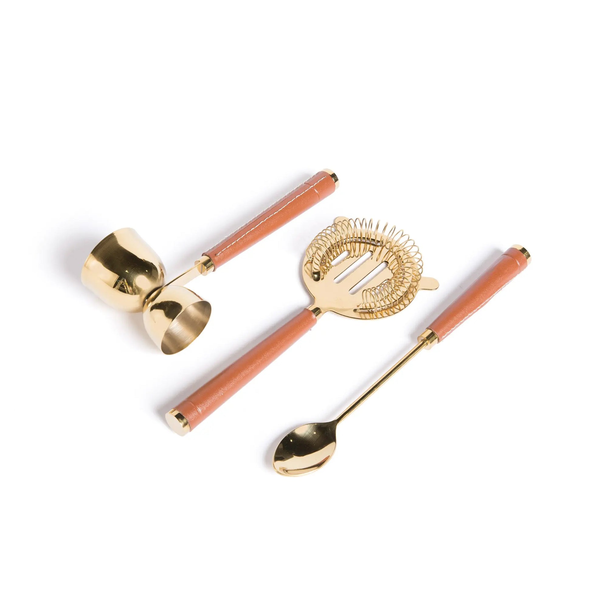 A set of gold-colored brass bar tools with leather handles, including a jigger, strainer, and spoon.