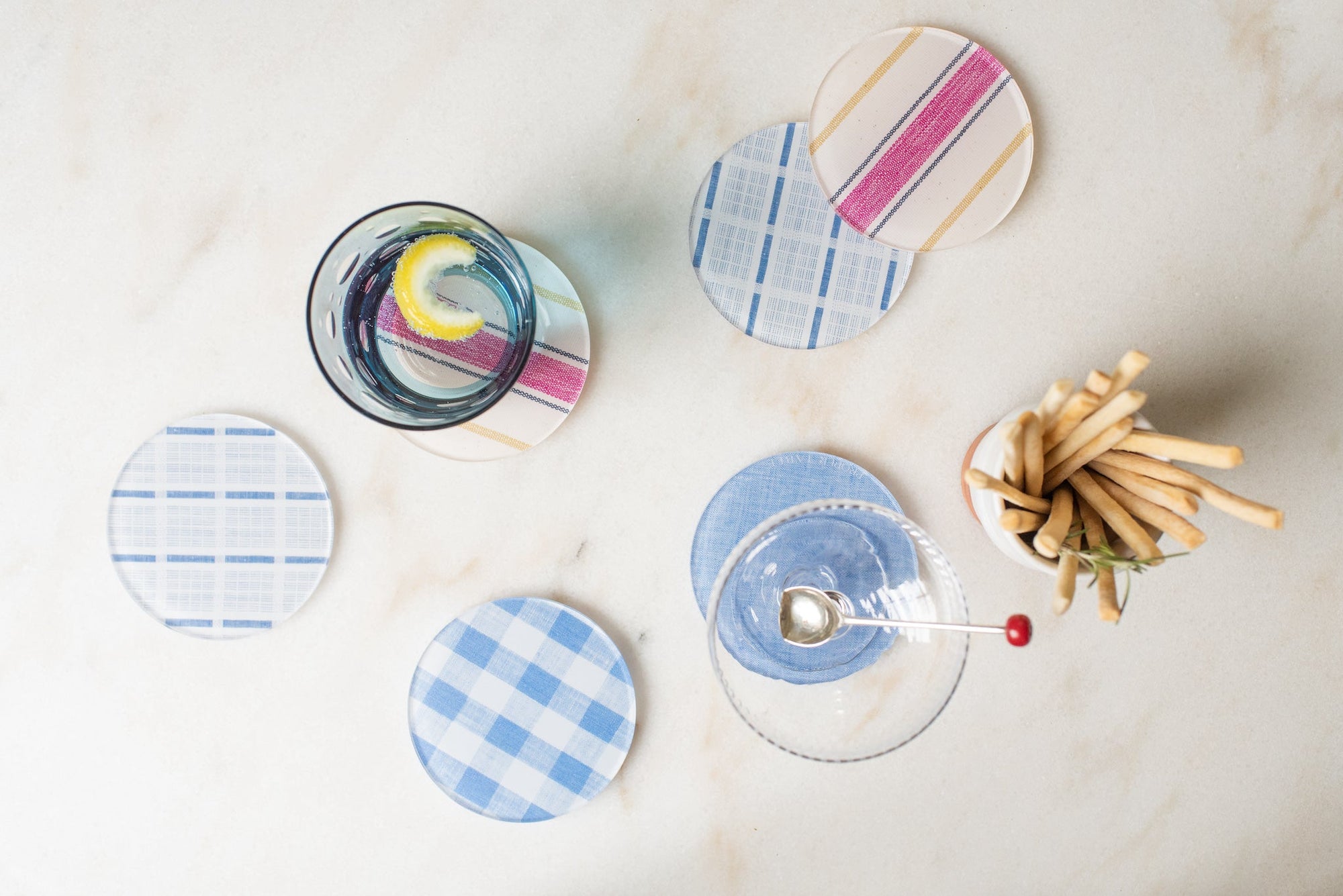 Set of colorful coasters on a marble surface with a bowl of breadsticks.