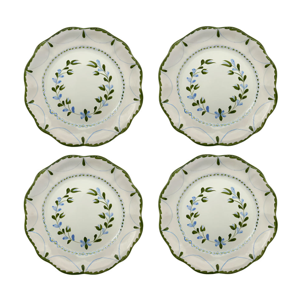 A set of four round ceramic dinner plates with a hand-painted floral pattern and green scalloped edges.