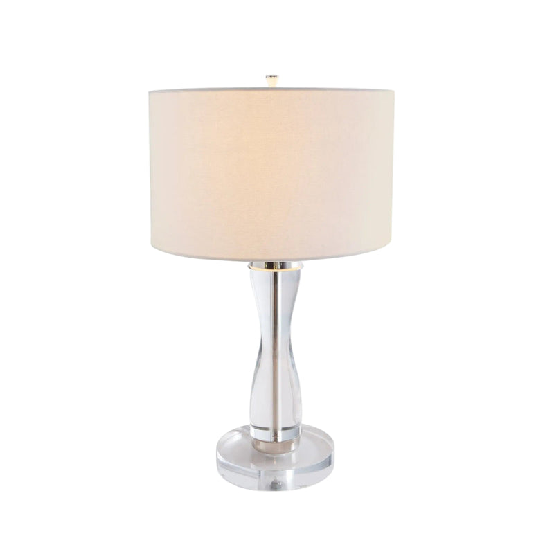 Table lamp with a beige shade and clear cylindrical base on a white background