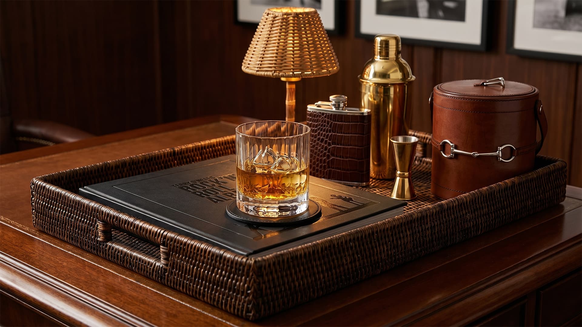 Tray with a glass of whiskey, lamp, and bar tools on a wooden surface.