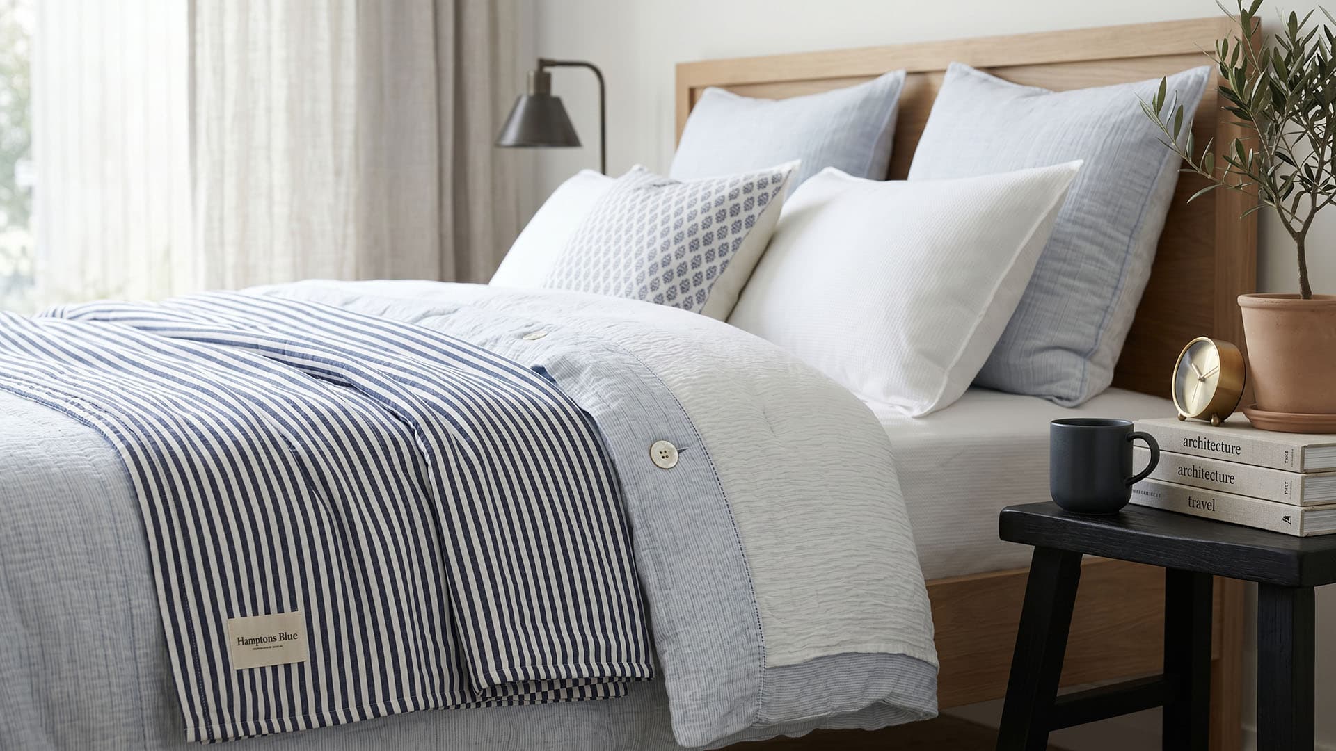 Bedroom with a neatly made bed featuring striped blanket and pillows, next to a nightstand with a cup.