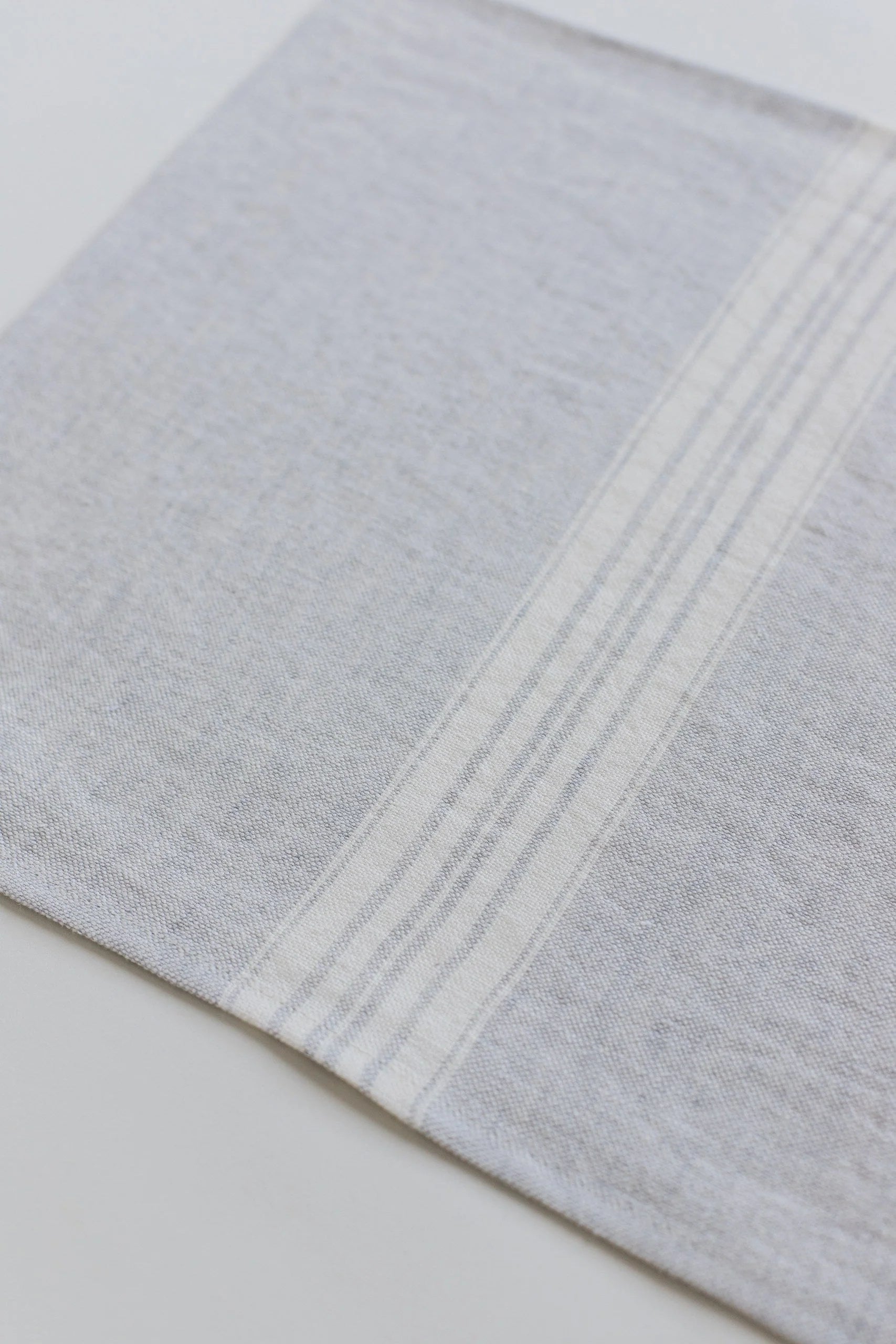 Close-up of a light gray linen placemat with subtle stripes on a white background