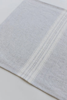 Close-up of a light gray linen placemat with subtle stripes on a white background
