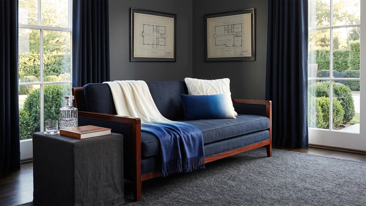 Blue sofa with white and blue cushions in a room with dark walls and large windows.