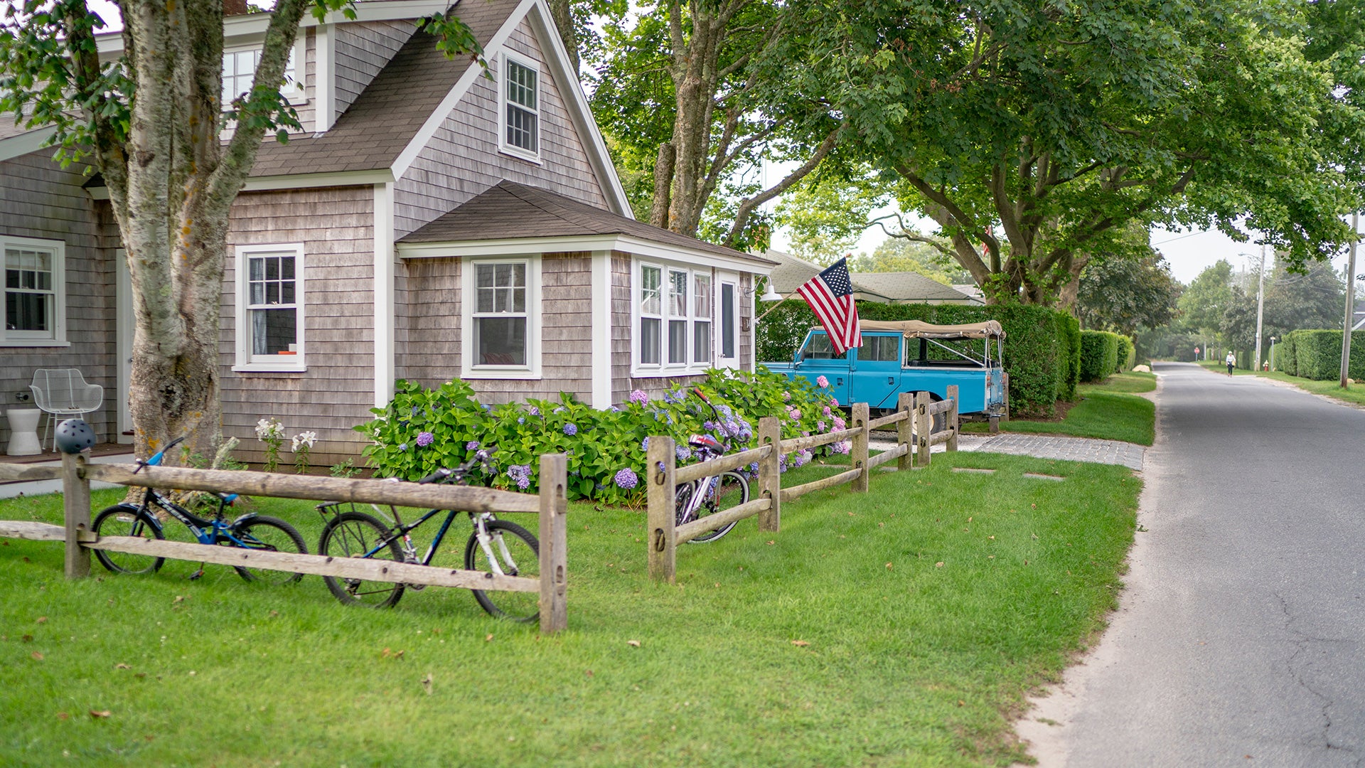 Cottage with bicycles, American flag, and blue truck on a residential street.