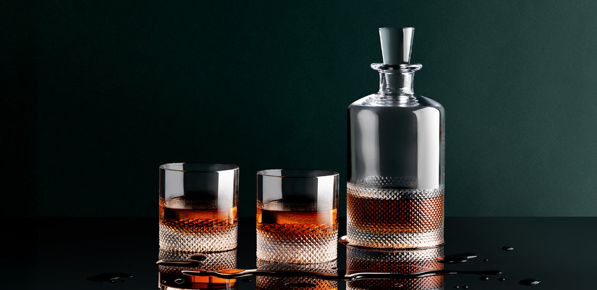 Whiskey decanter and glasses on a dark surface with a dark background