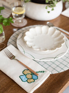 Dining table setting with a decorative plate, fork, placemat and embroidered napkin.