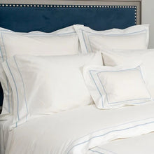 White pillows with blue stitching on a bed with a blue headboard.
