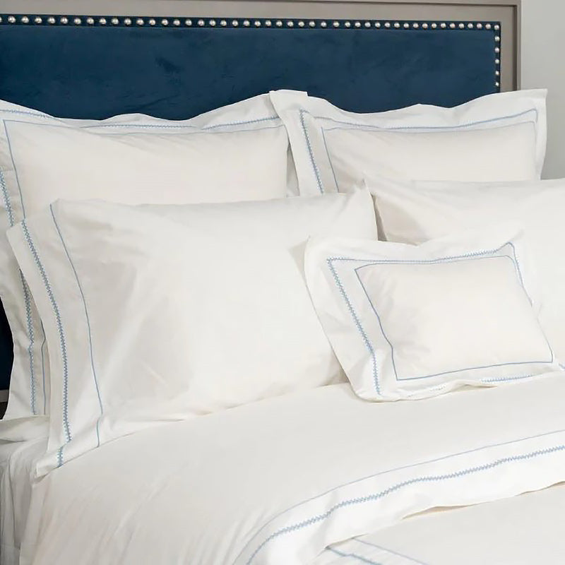 White pillows with blue stitching on a bed with a blue headboard.