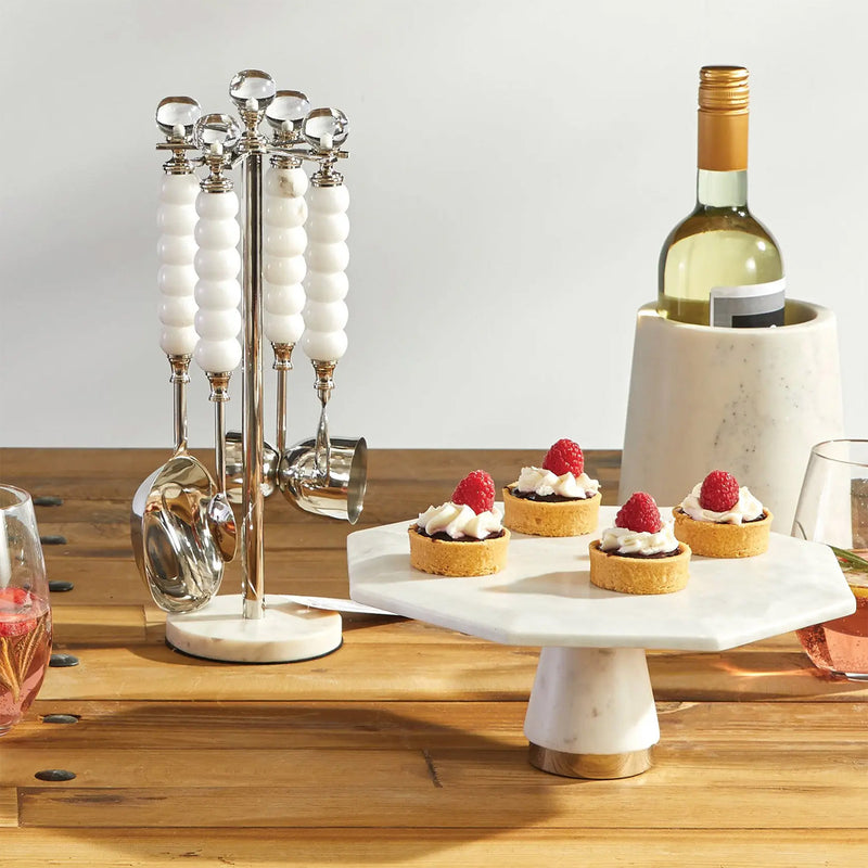 Decorative stand with small desserts and a bottle of wine on a wooden table.