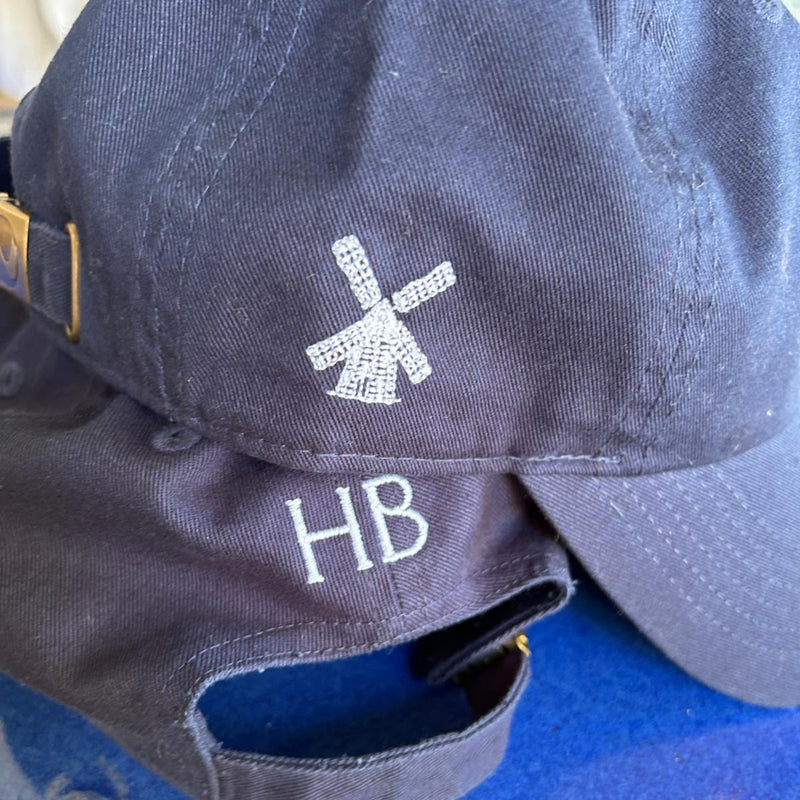 Navy blue cap with white logo and 'HB' text on a clear stand