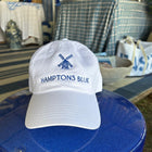 White cap with 'Hamptons Blue' logo on a blue stool outdoors.