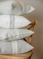 Stack of pillows with subtle stripes on a wooden chair against a neutral background