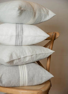 Stack of pillows with subtle stripes on a wooden chair against a neutral background
