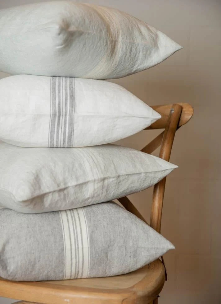Stack of pillows with subtle stripes on a wooden chair against a neutral background