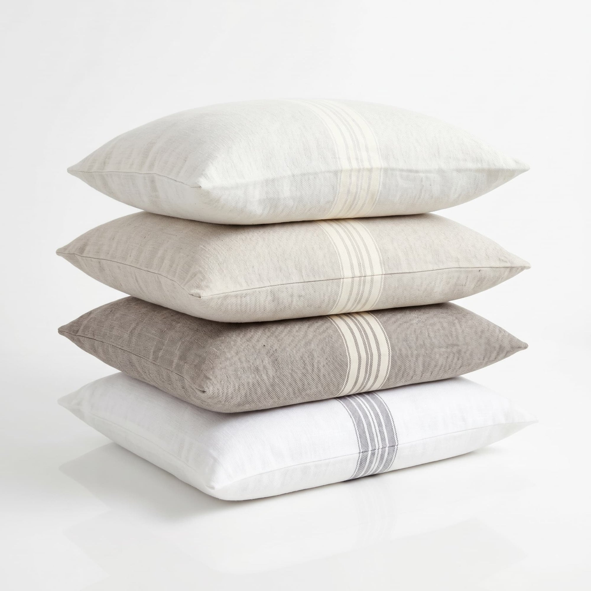 Stack of four pillows in white, beige, and gray on a light background