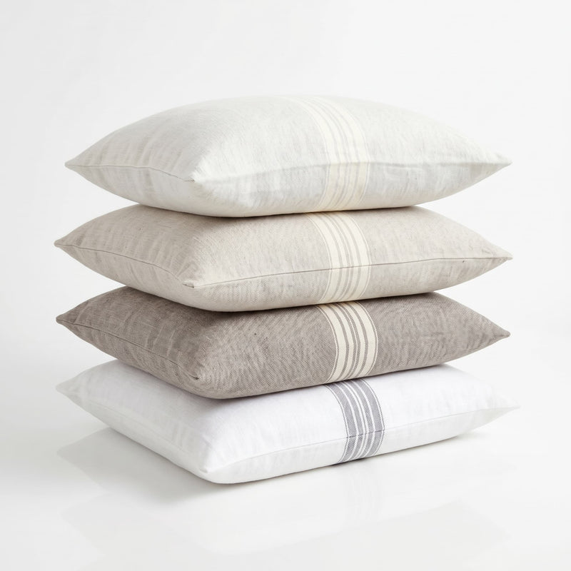 Stack of four pillows in white, beige, and gray on a light background