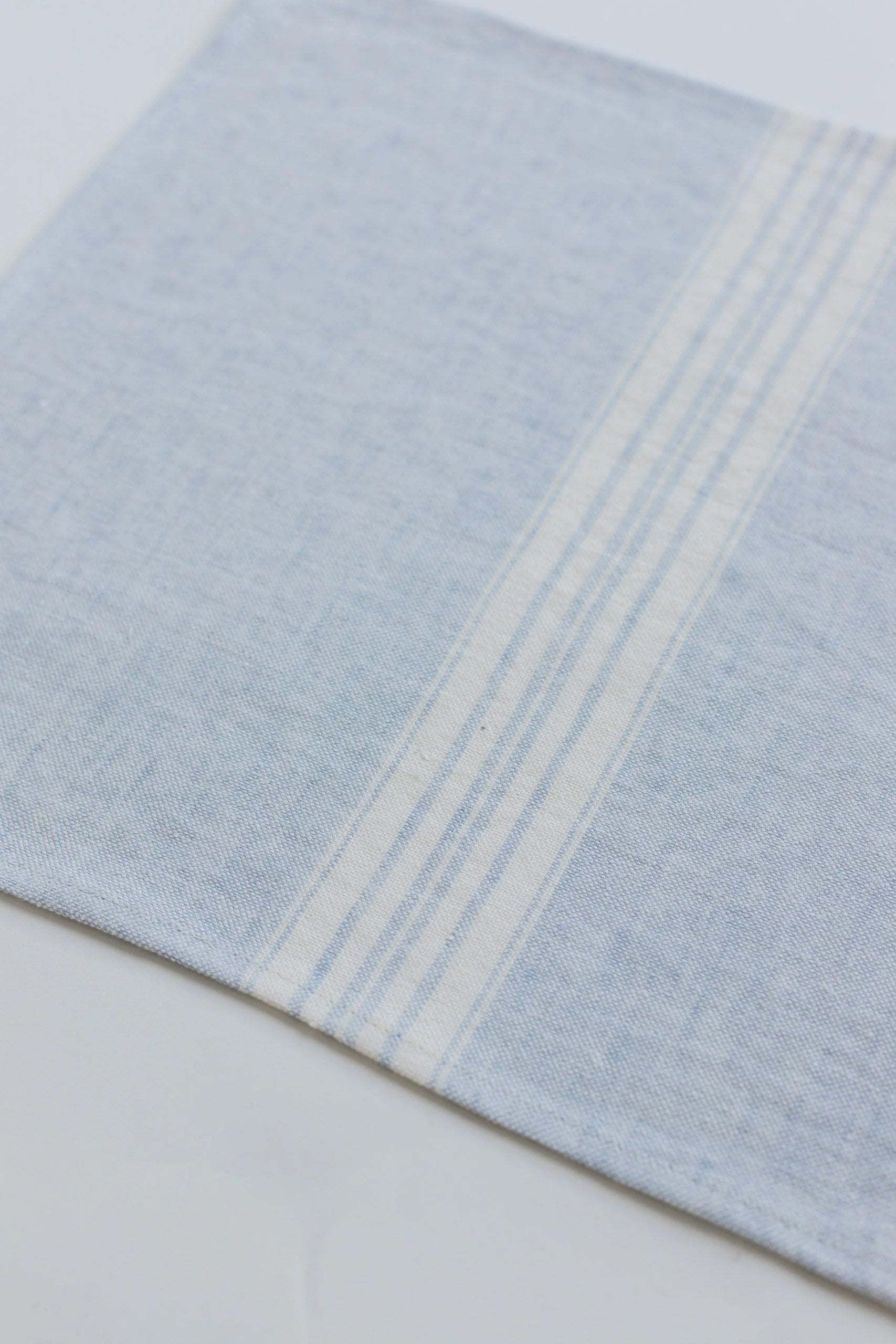 Close-up of a light blue linen placemat with white stripes on a beige background