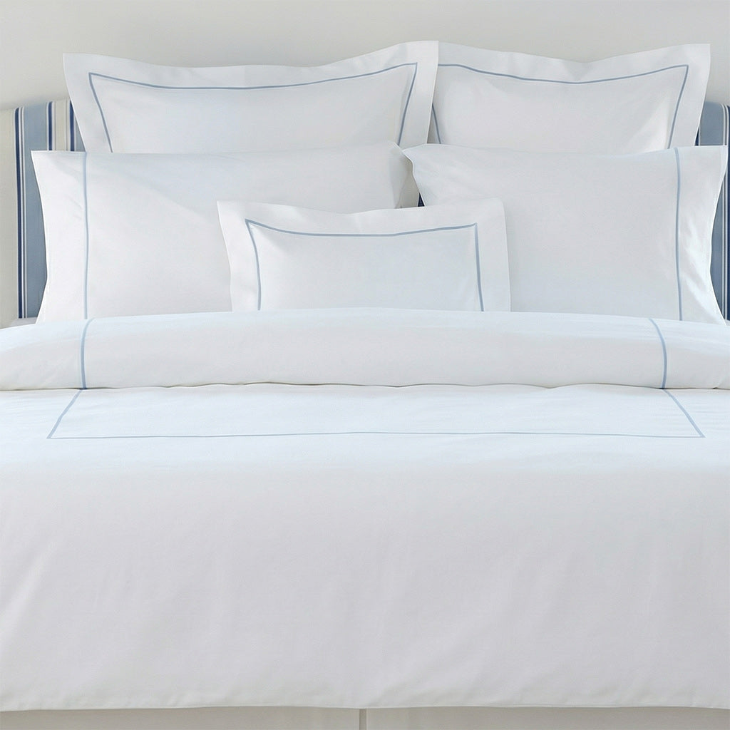 White bedding set with blue piping on a bed with a gray headboard.