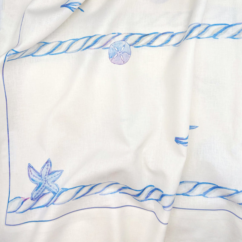 White fabric with blue embroidered designs of sand dollars and starfish on a white background
